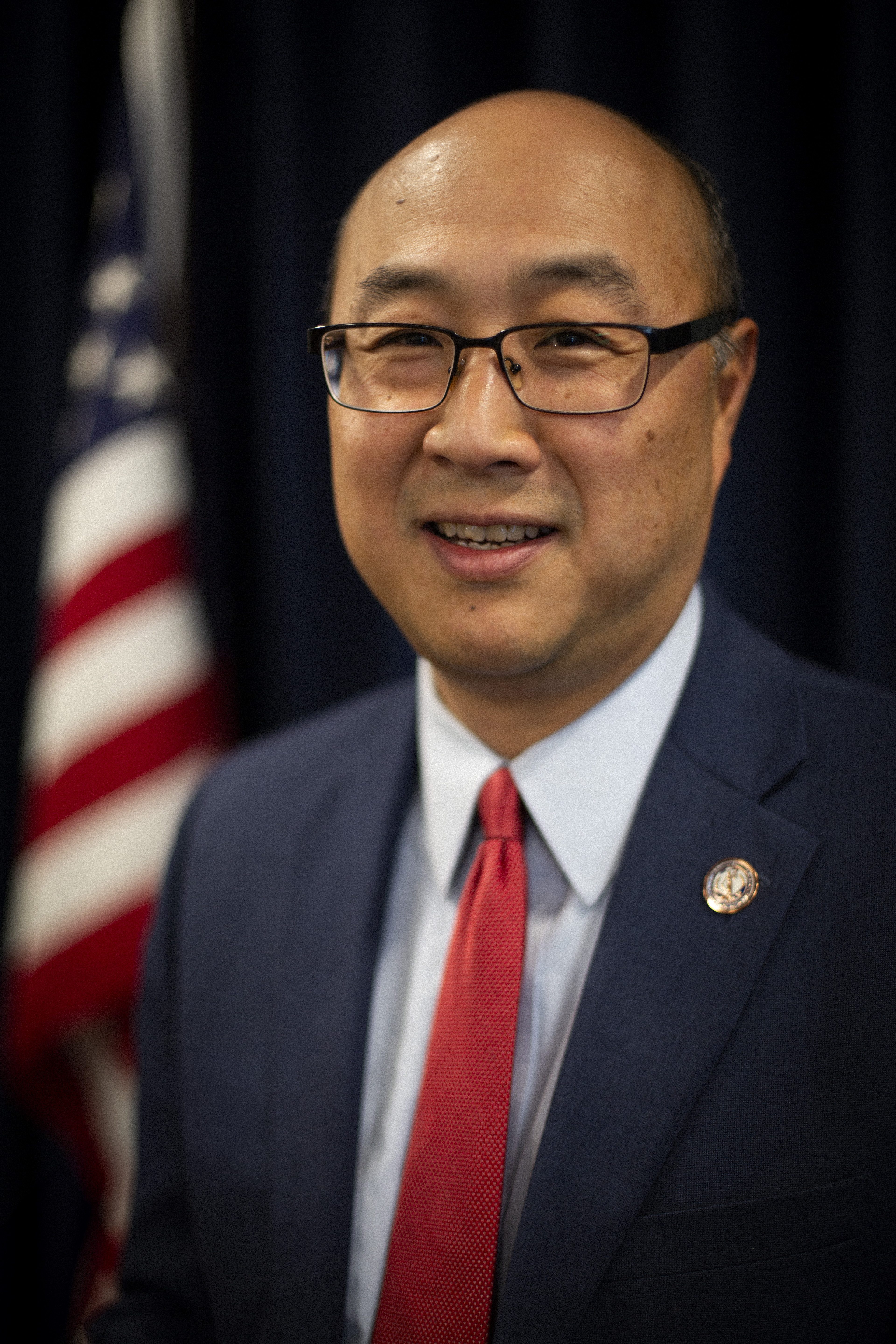 Headshot of John Choi smiling next to flag