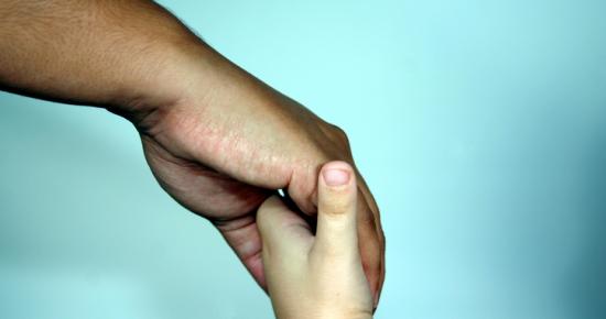 A closeup on a child's hand holding onto an adult's