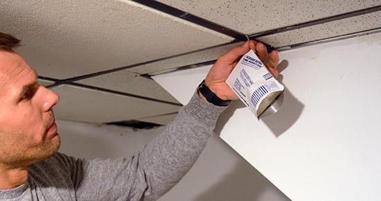 Man placing a radon test kit on a ceiling tile