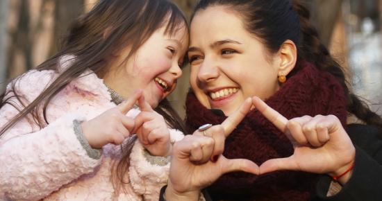 Two sisters smiling and making hand signs together