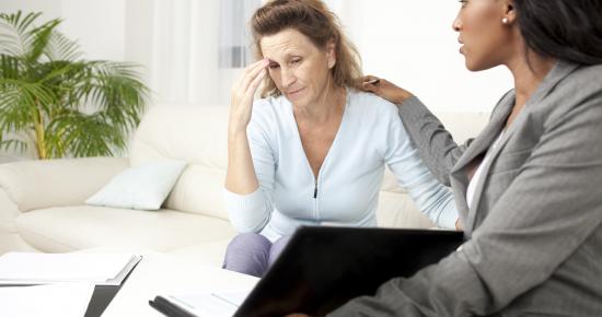 A woman looking concerned with her head in her hand, getting comforted by another woman